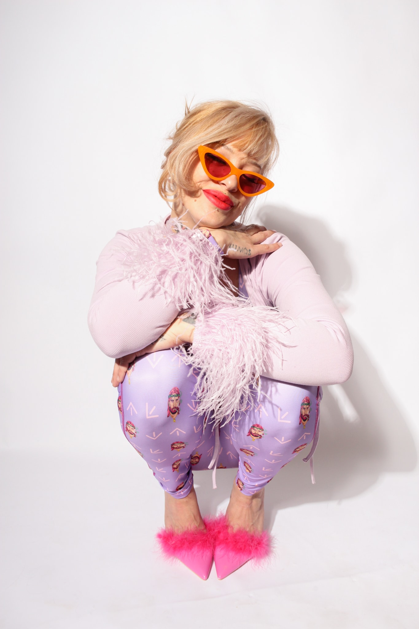South North Southwest crouching with arms folded and a lilac feather boa draped across